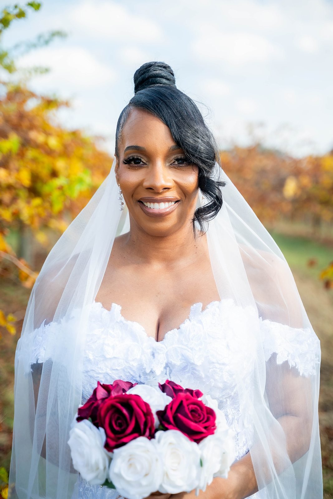 Bride smiles warmly holding red and white roses, her sheer veil framing her face and shoulders